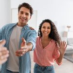 Happy young couple inviting people to enter home, shaking hands